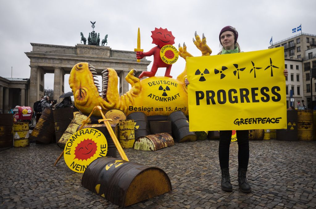 Aktivis Greenpeace berpose dengan poster di depan tiruan dinosaurus di depan Gerbang Brandenburg selama rapat umum menandai penutupan nuklir di Jerman di Berlin, Jerman, Sabtu (15/4/2023). 