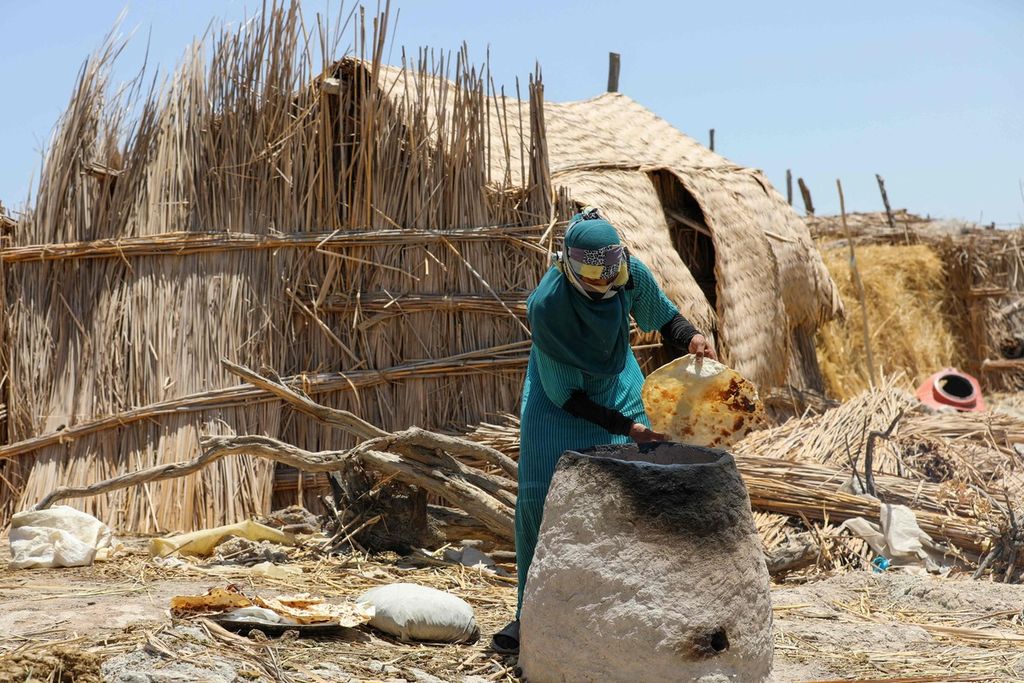 Seorang ibu tengah memanggang roti dalam tungku tanah liat di luar rumahnya di rawa Chibayish, Dhi Qar, Irak pada Kamis (22/6/2023).