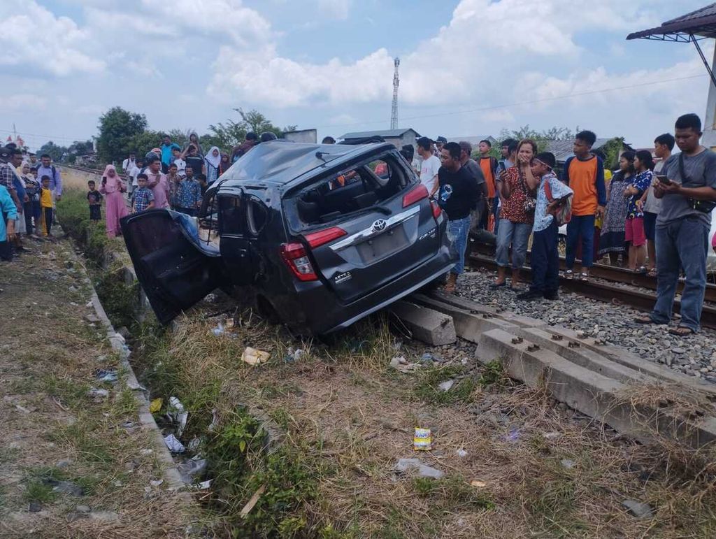 Warga melihat mobil yang tertabrak kereta api di perlintasan sebidang tidak terjaga di Jalan Lama, Kota Tebing Tinggi, Sumatera Utara, Rabu (16/8/2023). 