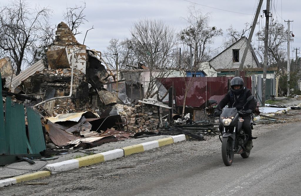 Seorang pria mengendarai sepeda motor melewati sebuah rumah yang hancur di desa Moshchun, barat laut Kyiv, Ukraina, Rabu (20/4/2022). Lebih dari satu juta orang Ukraina telah kembali ke negara mereka sejak invasi Rusia dimulai, kata seorang juru bicara pasukan perbatasan Kyiv.