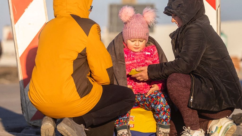 Seorang anak ditemani orangtuanya menghangatkan diri di tengah cuaca dingin yang menyengat di perbatasan Ukraina-Polandia, Senin (28/2/2022). Lebih dari 660.000 warga Ukraina telah menyerbu perbatasan untuk menyeberang ke Polandia, Moldova, Hongaria, Romania, dan Slowakia. Diperkirakan jumlah pengungsi akan terus bertambah. 