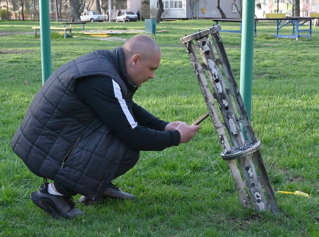 Warga memotret pecahan rudal di lapangan dekat permukiman di Kharkiv, Ukraina, 15 April 2022. Rusia melancarkan serangan di kota itu yang menewaskan tujuh orang dan melukai 34 orang lainnya, menurut laporan otoritas setempat. 