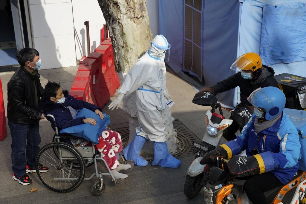 Pekerja medis yang mengenakan baju pelindung mengawal seorang pasien dengan kursi roda di Rumah Sakit Tongji, Wuhan, Provinsi Hubei, China, Jumat (15/1/2021). Tim peneliti yang diutus WHO telah berada di Wuhan untuk memulai mengumpulkan data dan mencari petunjuk mengenai awal pandemi Covid-19.