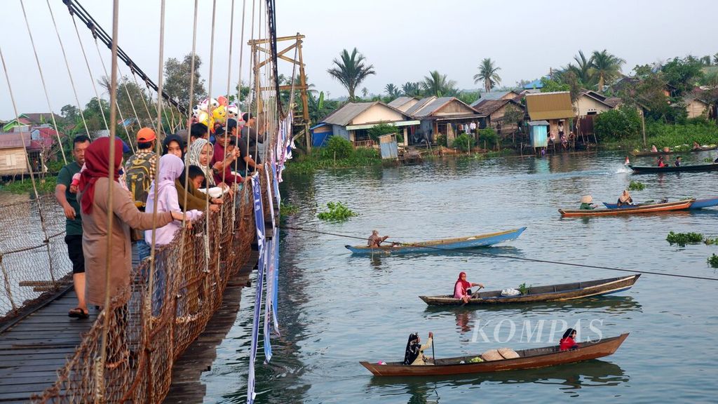 Pengunjung menyaksikan kegiatan Festival Pasar Terapung Lok Baintan Tahun 2023 dari atas Jembatan Gantung Lok Baintan, Sungai Tabuk, Kabupaten Banjar, Kalimantan Selatan, Minggu (19/11/2023). 