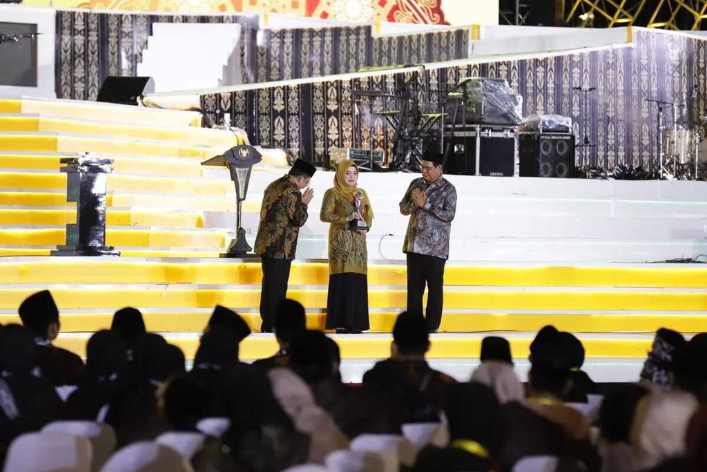 Qariah asal Kalimantan Selatan, Raudhah (tengah), menerima piala qariah terbaik MTQ Nasional XXIX Tahun 2022 dari Wakil Menteri Agama Zainut Tauhid Sa’adi (kiri) pada acara penutupan MTQ Nasional di Astaka Utama Kiram Park, Kabupaten Banjar, Selasa (18/10/2022) malam.