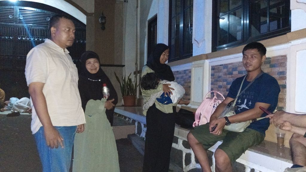 Wahyu (28) bersama keluarga menumpang di teras rumah warga, Sabtu (14/4/2024) malam. Pemberlakuan sistem satu arah selama 12 jam menyebabkan kendaraan keluarga ini tertahan.