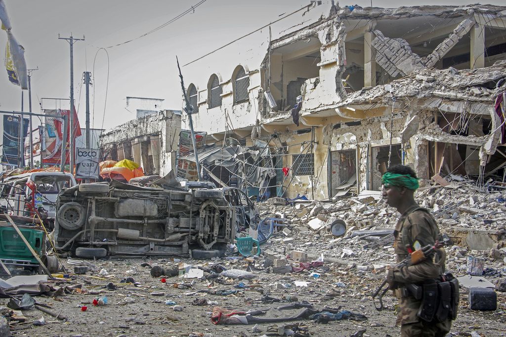 Seorang anggota militer melewati bangunan dan kendaraan yang rusak berat di lokasi ledakan bom mobil di Mogadishu, Somalia, Sabtu (29/10/2022). Serangan bom mobil ini menewaskan 100 orang dan melukai 300 orang. 