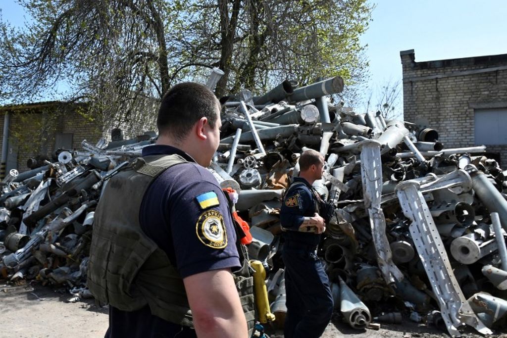 Dua personil Layanan Darurat Negara Ukraina berdiri di depan tumpukan sisa-sisa rudal, Rusia yang dikumpulkan setelah penembakan di Kharkiv, Senin, 25 April 2022, di tengah perang Rusia ke Ukraina. 