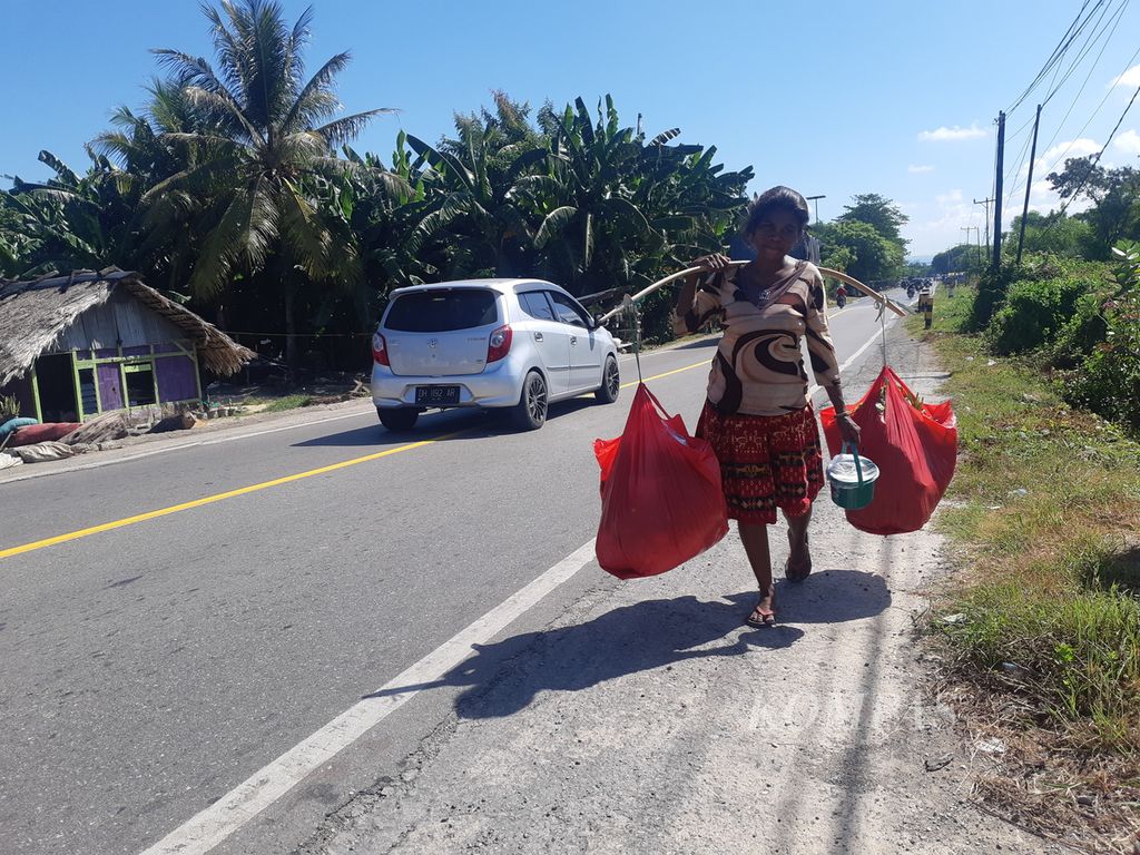 Pedagang sayur keliling berjalan menjajakan jualannya di sisi Jalan Timor Raya tepatnya Desa Tanah Merah, Kabupaten Kupang, Nusa Tenggara Timur, Selasa (13/12/2022). Pedagang itu menggambarkan kegigihan orang miskin yang berjuang demi hidup keluarga mereka.