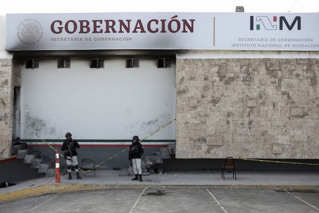 Dua polisi berjaga-jaga di depan pintu masuk Pusat Penampungan Migran di kota Ciudad Juarez, Meksiko, Selasa (28/3/2023). Kebakaran di lokasi itu mengakibatkan 38 migran pencari suaka tewas dan puluhan orang lainnya terluka. 