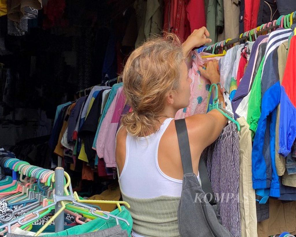Seorang wisatawan asing sedang berbelanja pakaian bekas (<i>thrifting</i>) di Pasar Kodok, Tabanan, Bali, Minggu (29/1/2023).