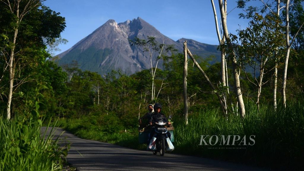 Warga melintasi jalan dengan latar belakang puncak Gunung Merapi di Desa Glagaharjo, Cangkringan, Kabupaten Sleman, DI Yogyakarta, pada Desember 2018.