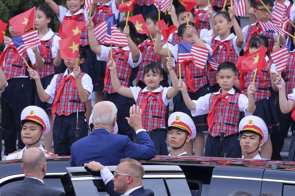 Presiden Amerika Serikat Joe Biden (tengah) melambaikan tangan kepada siswa yang berdiri sambil mengayunkan bendera AS dan Vietnam saat tiba di Istana Kepresidenan di Hanoi, Vietnam, Minggu (10/9/2023). AS dan Vietnam menaikkan status hubungan bilateral keduanya ke level kemitraan strategis komprehensif.  