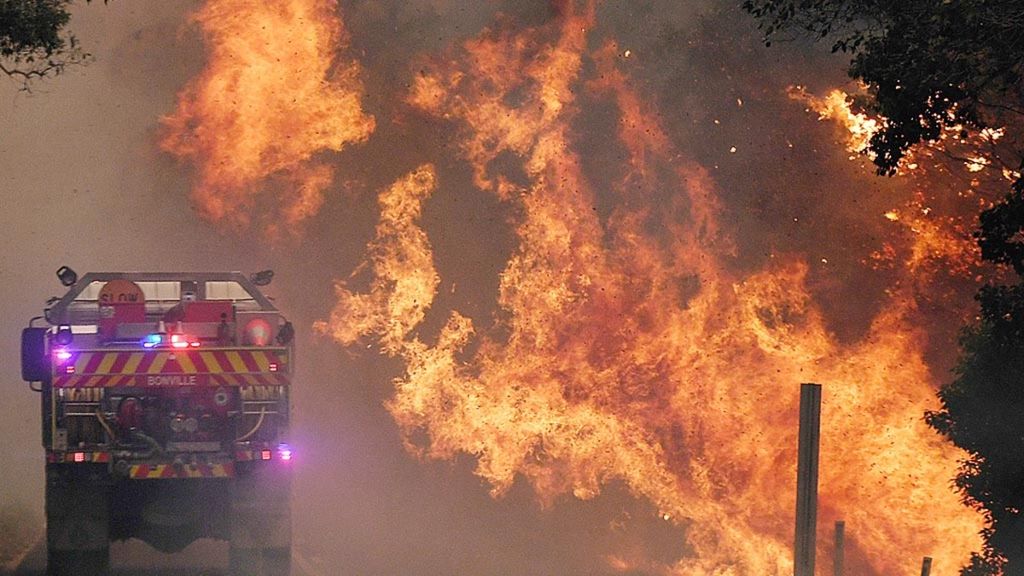 Truk pemadam kebakaran berada tak jauh dari kobaran api kebakaran hutan di Nana Glen, dekat Coffs Harbour, Australia, 12 November 2019.