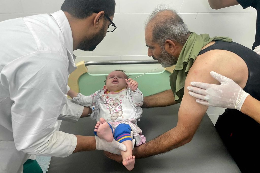 Seorang dokter dan seorang pria di Rumah Sakit Kuwait, Rafah, Jalur Gaza selatan, 21 Oktober 2023, mengangkat seorang bayi yang terluka akibat gempuran Israel di Jalur Gaza. 