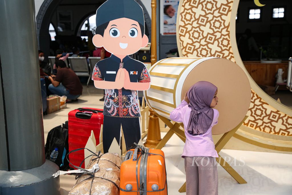 Seorang anak yang mudik bersama orang tuanya berfoto dengan latar belakang dekorasi Lebaran di Stasiun Pasar Senen, Jakarta Pusat, Kamis (13/4/2023). Para pemudik yang membawa anak memilih mudik lebih awal untuk menghindari keramaian di perjalanan.