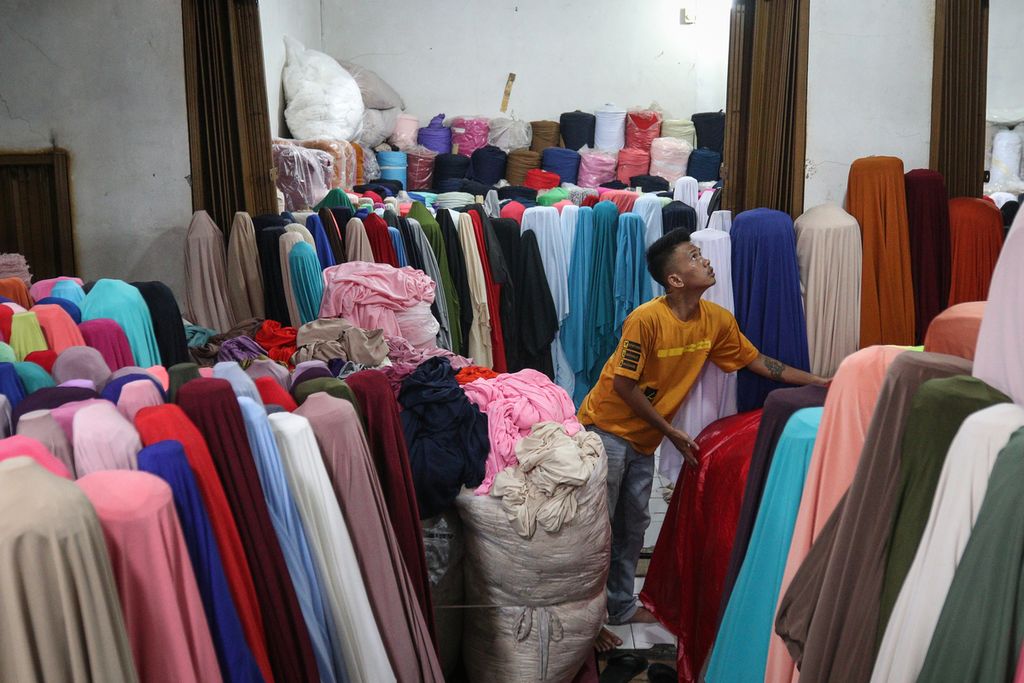 Seorang pedagang menutupi kain dengan plastik agar terhindar dari hujan di Pasar Cipadu, Tangerang, Kamis (3/11/2022). Kawasan Cipadu dikenal sebagai sentra perdagangan tekstil di Tangerang. Di tengah lesunya permintaan, para pedagang tekstil tetap bertahan dengan berbagai cara. 