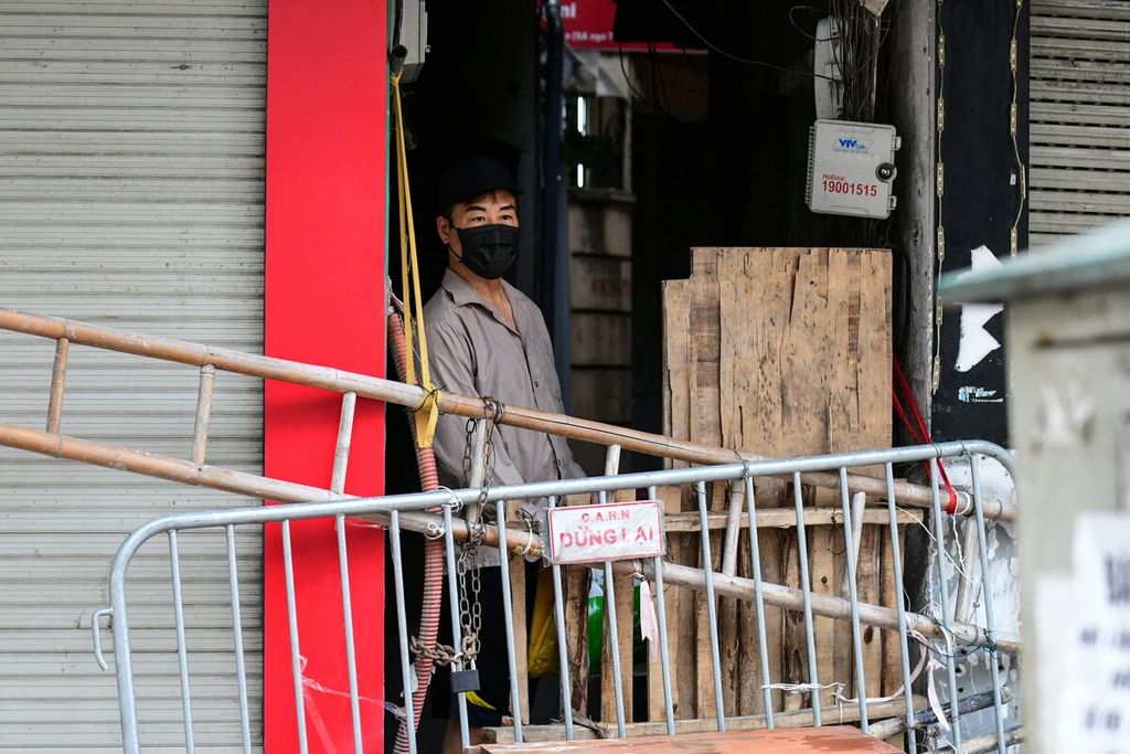 Warga berdiri di belakang barikade yang dipasang di salah satu pusat pertokoan di Hanoi, Vietnam, Rabu (25/8/2021). Karantina wilayah dan pembatasan ketat di Hanoi kembali diperpanjang.