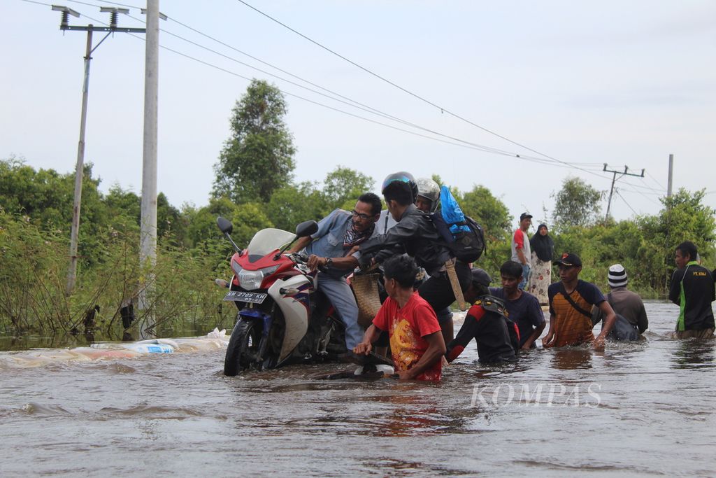 Warga Desa Lembeng, Kecamatan Dusun Selatan, Kabupaten Barito Selatan, Kalteng, membantu pengendara yang ingin melintas di titik banjir jalur Trans-Kalimantan yang menghubungkan tiga provinsi pada Kamis (25/1/2024).