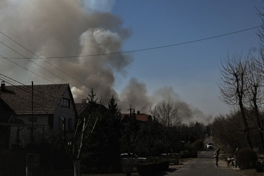Tentara Ukraina menjaga pos pemeriksaan saat asap mengepul setelah serangan Rusia di kota Novi Petivtsy, utara Kyiv, pada 19 Maret 2022. 