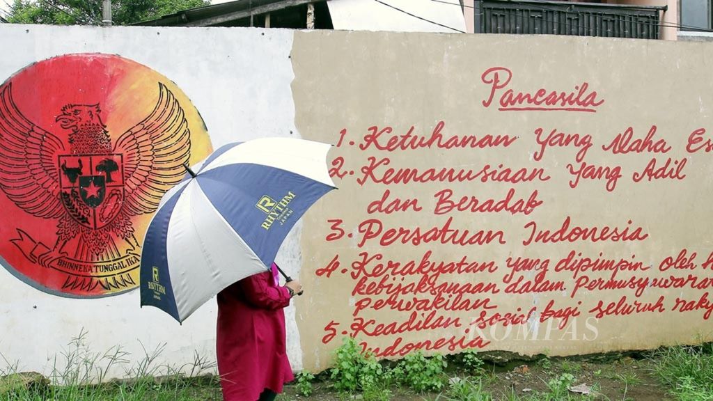 Seorang perempuan melintas di dekat dinding yang berhiaskan mural Garuda Pancasila di kawasan Pasar Minggu, Jakarta, Minggu (2/2/2020).  Mural tersebut mengingatkan kita sebagai orang Indonesia untuk mengalmalkan nilai-nilai Pancasila dalam kehidupan berbangsa dan bernegara. 