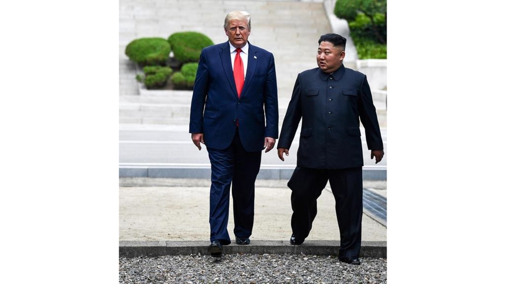 Pemimpin Korea Utara Kim Jong Un dan Presiden Amerika Serikat Donald Trump berjalan bersama melewati garis demarkasi yang memisahkan Korea Utara dan Korea Selatan setelah pertemuan singkat mereka di Panmunjom, Minggu (30/6/2019).