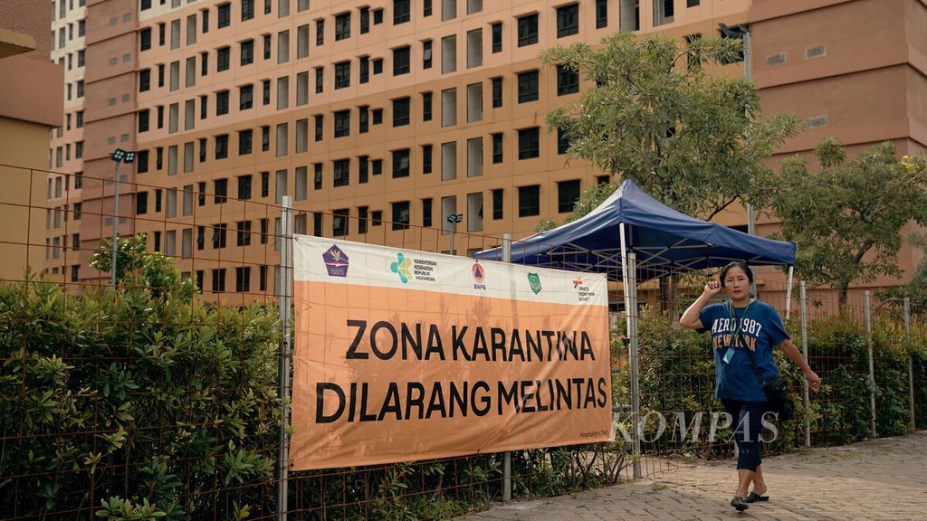 Warga melintasi batas zona karantina di Rumah Susun Nagrak, Cilincing, Jakarta Utara, Minggu (9/1/2022). Kasus baru penularan Covid-19 varian Omicron terus bertambah. 