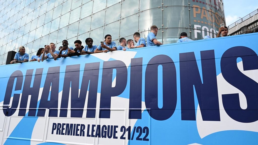 Para pemain Manchester City berdiri di atas bus bak terbuka saat mengikuti parade kemenangan berkeliling kota Manchester. The Citizens menjuarai Liga Inggris musim ini setelah meraih 26 kemenangan, 6 kali seri, dan hanya mengalami 3 kekalahan dalam satu musim ini. 
