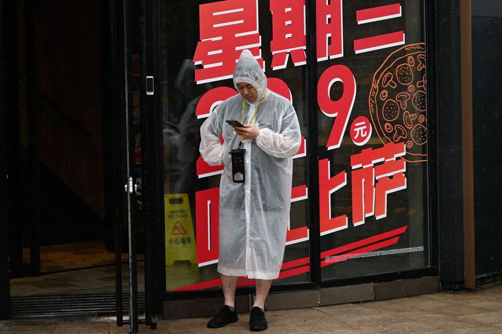 Seorang warga berlindung dari derasnya hujan di Beijing, China pada Minggu (30/7/2023). Sebagian wilayah China sejak Jumat lalu diterjang topan Doksuri.