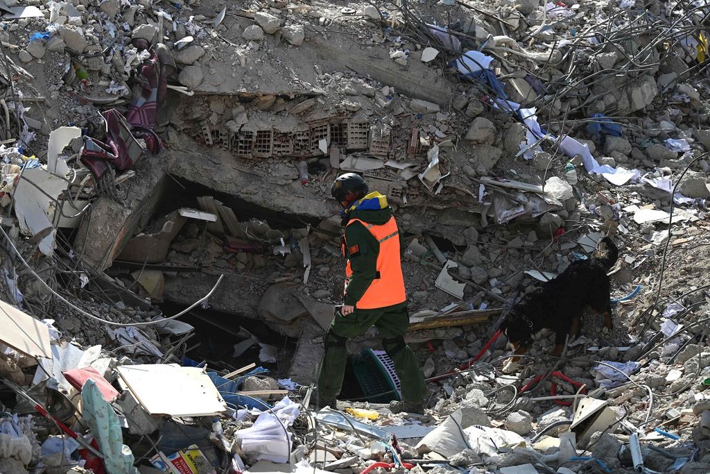 Seorang anggota tim SAR bersama seekor anjing pelacak mencari lokasi korban gempa di reruntuhan bangunan di Kahramanmaras, Selasa (14/2/2023).