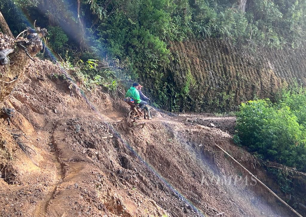 Pengendara sepeda motor berjalan di sisi tebing yang longsor di jalur Mabusa-Se'pon, Di Seko, Luwu Utara, Sulawesi Selatan, Senin (4/7/2022).
