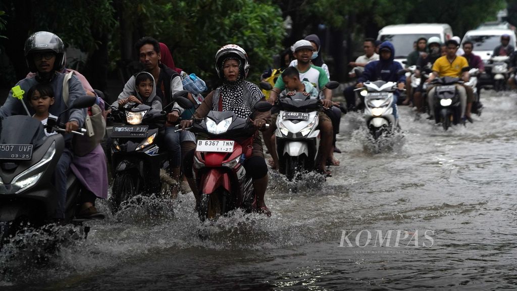 Warga melintasi genangan air akibat curah hujan tinggi di Jalan Kramat Jaya Raya, Cilincing, Jakarta Utara, Minggu (1/1/2023). Hujan deras yang mengguyur sejak Minggu (1/1/2023) pagi membuat sejumlah jalan tergenang hingga kedalaman 30 sentimeter.