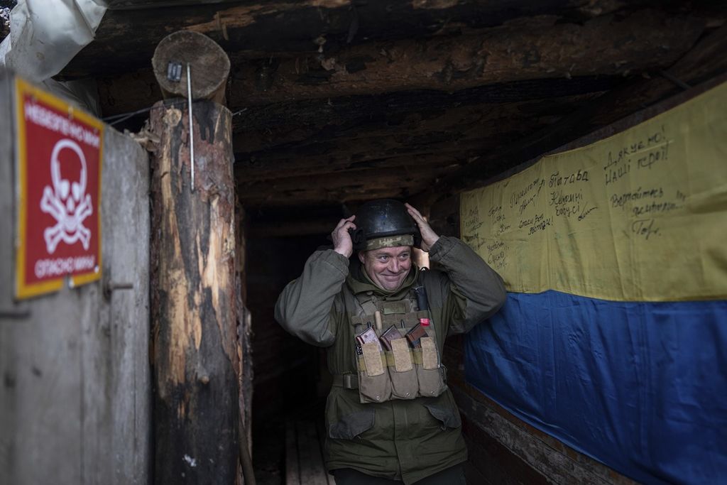 Seorang prajurit Ukraina tersenyum memasuki tempat penampungan yang dihiasi dengan bendera nasional Ukraina setelah berakhir tugasnya di posisi garis depan dekat Zolote, Ukraina, Senin (7/2/2022).