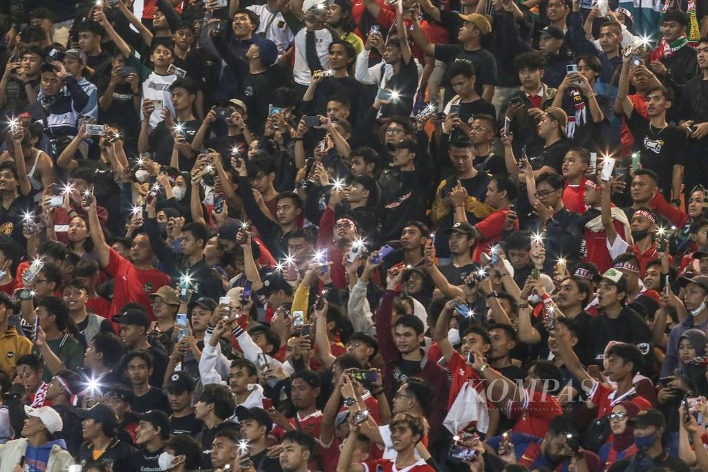 Penonton menyalakan lampu gawainya saat mendukung tim nasional Indonesia melawan Curacao dalam laga uji coba di Stadion Pakansari, Cibinong, Bogor, Jawa Barat, Selasa (27/9/2022). Indonesia dikenal sebagai negara yang gila bola. Mayoritas penduduknya menggemari sepak bola. 