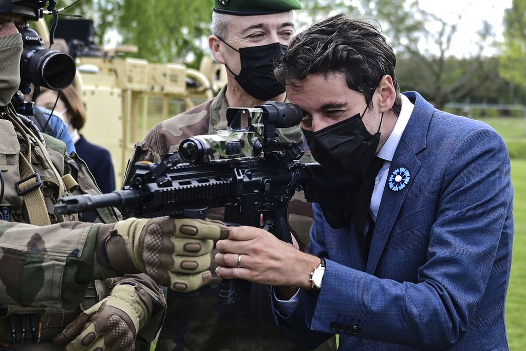 Juru Bicara Menteri Luar Negeri dan Pemerintah Perancis Gabriel Attal memegang senapan mesin saat berkunjung ke kamp militer Satory di Versailles-Satory, sebelah barat Paris, 7 Mei 2021.