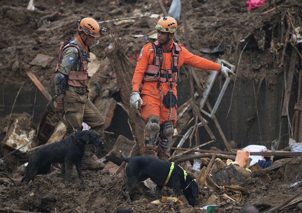 Anggota tim SAR dari Dinas Pemadam Kebakaran dibantu oleh anjing pelacak mencari penyintas  di antara reruntuhan rumah warga yang tertimbun tanah longsor di Petropolis, Brasil, Rabu (16/2/2022).