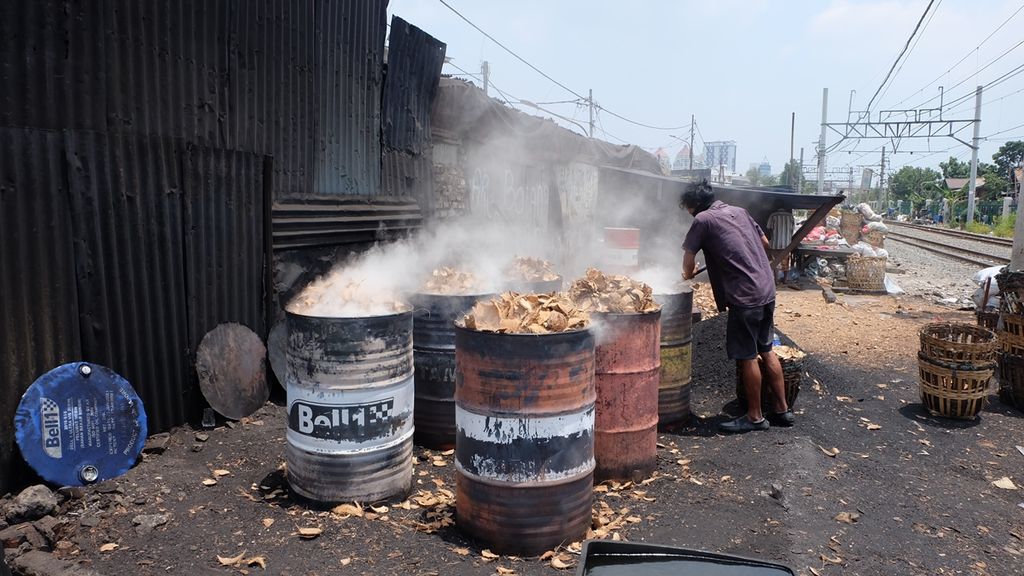 Pekerja membakar batok kelapa untuk dijadikan arang di pinggir rel kereta api di RW 006 Kelurahan Tanah Tinggi, Kecamatan Johar Baru, Jakarta Pusat, Senin (16/9/2019).