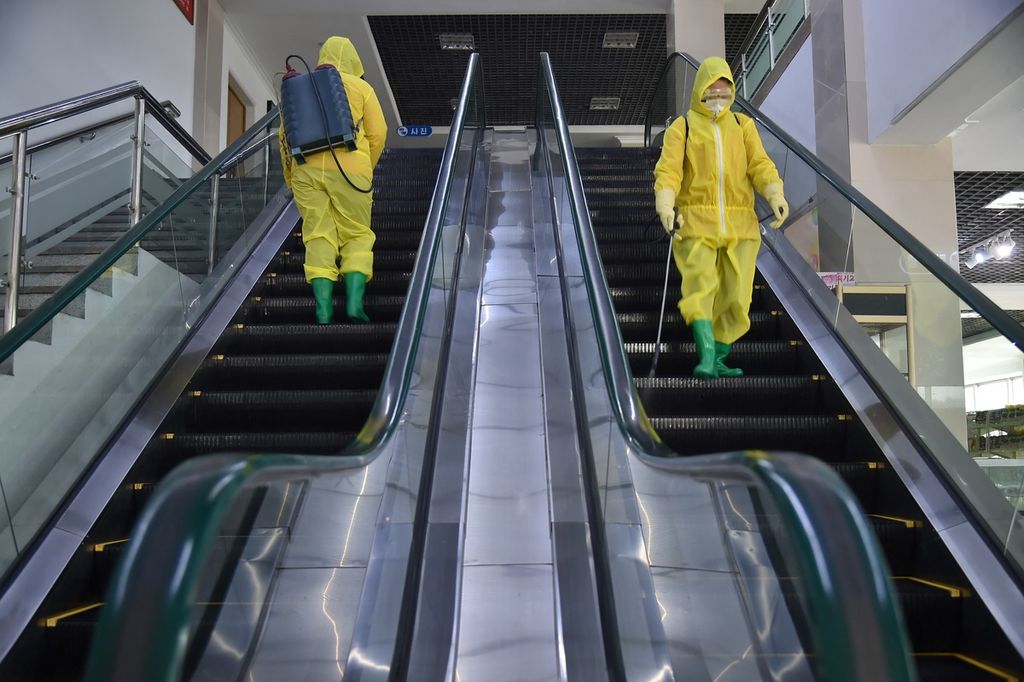 Foto yang diambil pada 18 Maret 2022 memperlihatkan dua petugas kesehatan tengah menyemprotkan cairan disinfektan ke lantai eskalator sebuah supermarket di Pyongyang, Korut. Pemerintah Korut, Kamis (12/5/2022), secara resmi mengumumkan adanya kasus Covid-19 pertama di negara itu setelah lebih dari dua tahun menutup pintu perbatasannya. 
