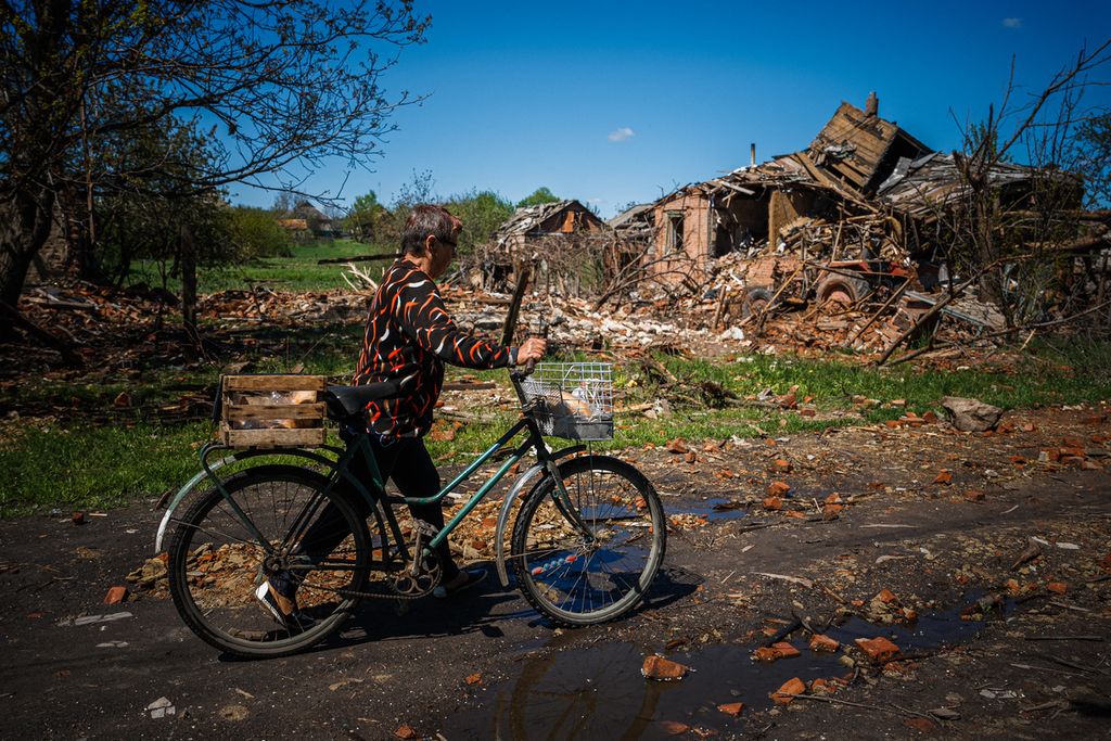 Valentyna Zaruba melewati sebuah rumah yang hancur saat ia membawa roti dengan sepeda untuk dibagikan kepada tetangga-tetangganya di Siversk, Donetsk, 2 Mei 2023, di tengah invasi Rusia ke Ukraina. 