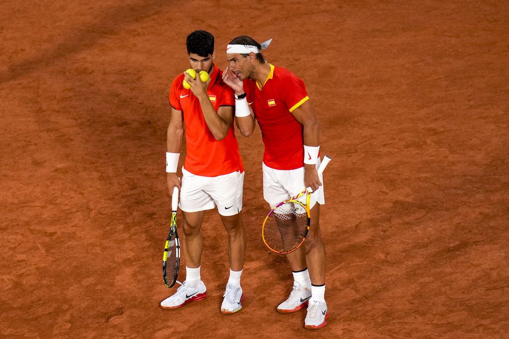 Petenis Spanyol Carlos Alcaraz (kiri) berbicara dengan Rafael Nadal saat bertanding pada nomor ganda putra tenis Olimpiade Paris 2024 melawan ganda Argentina, Andres Molteni/Maximo Gonzalez, di Roland Garros, Paris, Minggu (28/7/2024) dini hari WIB. 