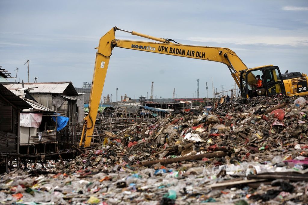 Ekskavator digunakan untuk mengeruk sampah yang telah menumpuk selama bertahun-tahun di lahan kosong sisa pembuatan tanggul laut di kawasan RW 005, Kelurahan Kalibaru, Cilincing, Jakarta Utara, Kamis (24/2/2022). Warga membuang sampah di lahan kosong tersebut sejak tanggul selesai dibuat. 
