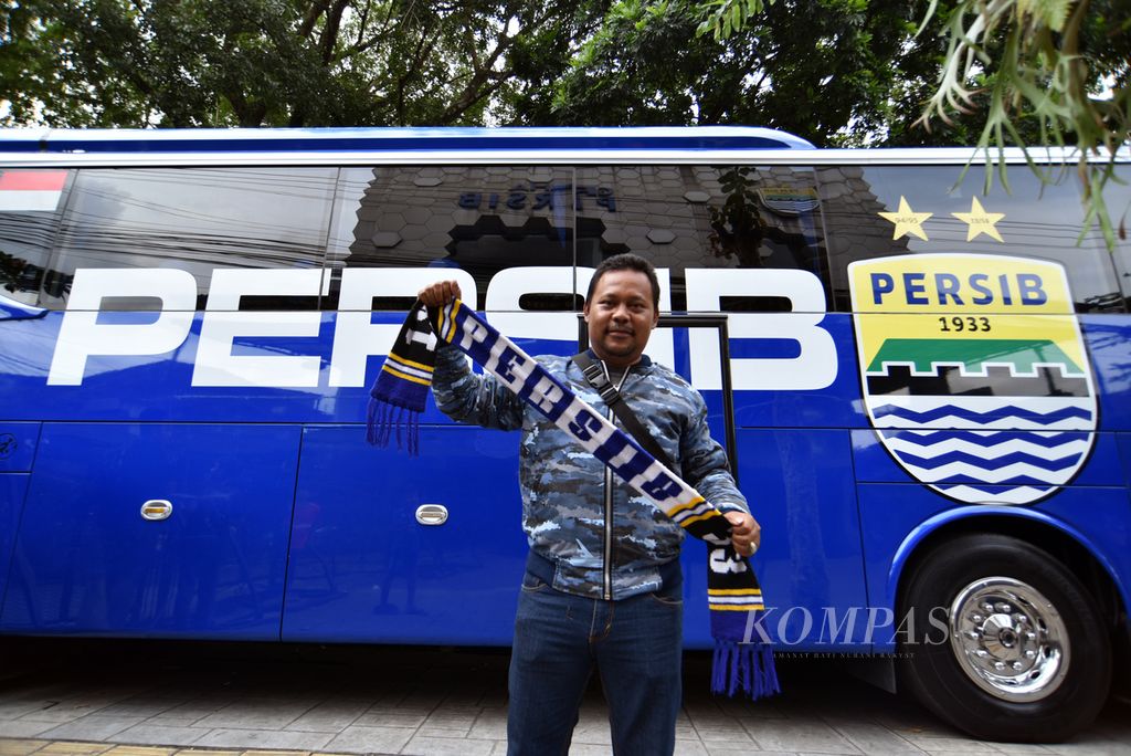 Penggemar Persib Bandung atau bobotoh asal Depok, Jawa Barat, Regi Hidayat, berfoto dengan latar belakang bus Persib di Graha Persib, Bandung, Jumat (14/7/2023). 