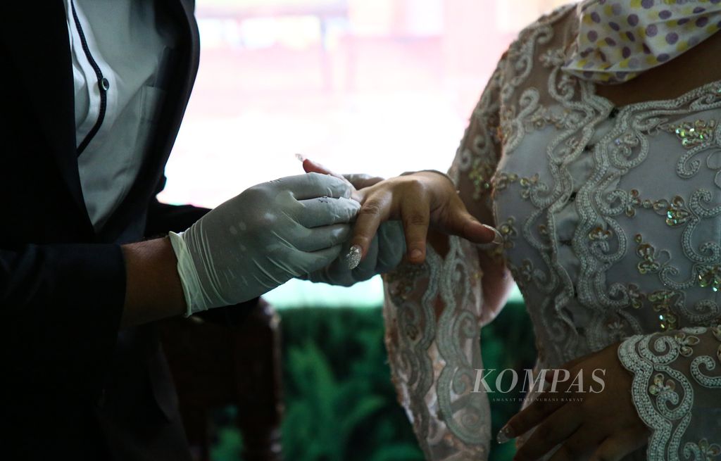 Rizki mengenakan sarung tangan saat memasangkan cincin pernikahan ke jari pasangannya, Mutiara, dalam acara pernikahan mereka di Kantor Urusan Agama (KUA) Kecamatan Gambir, Jakarta Pusat, Minggu (5/4/2020). Di tengah pandemi Covid-19, banyak pasangan akhirnya melaksanakan pernikahan secara sederhana di KUA. 
