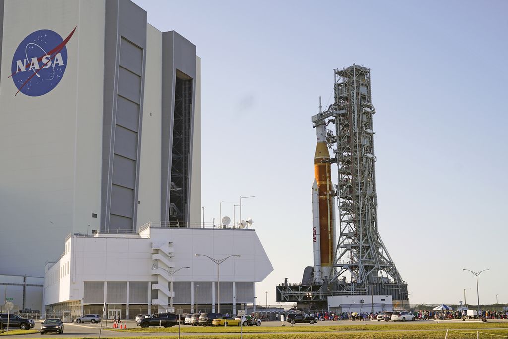 Roket NASA Artemis, kanan, dengan pesawat ruang angkasa Orion meninggalkan Gedung Perakitan Kendaraan bergerak perlahan dalam perjalanan 11 jam untuk meluncurkan landasan 39B di Kennedy Space Center di Cape Canaveral, Florida, Kamis, (17/3/2022). Saat berada di pad roket dan pesawat ruang angkasa Orion akan menjalani tes untuk memverifikasi sistem dan praktek prosedur hitung mundur. (Foto AP/John Raoux)