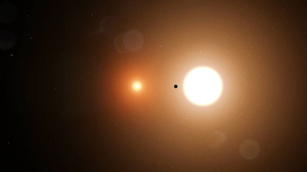 Planet TOI 1338 (hitam kecil ditengah) mengelilingi sistem bintang ganda yang terdiri atas sebuah bintang seukuran Matahari (kanan) dan bintang katai coklat (kiri). Sekitar 70 persen dari bintang-bintang di sekitar Matahari terbentuk sebagai multibintang, baik bintang ganda maupun bintang triplet.