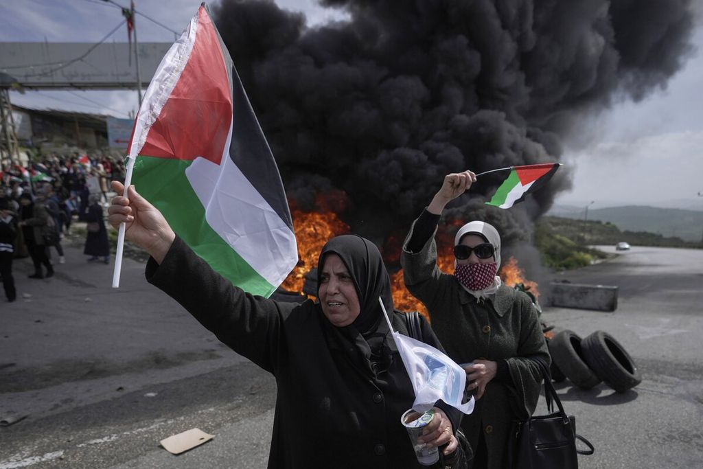 Dua perempuan mengibarkan bendera Palestina di Tepi Barat, Senin (7/3/2022). 