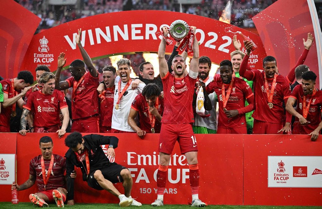 Kapten tim Liverpool, Jordan Henderson (tengah), memegang trofi juara Piala FA Inggris seusai mengalahkan Chelsea lewat adu penalti pada final, Sabtu (14/5/2022) di Stadion Wembley, London.