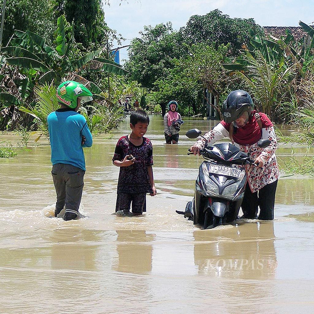 Warga menuntun motornya melintasi jalan poros Desa Sedapurklagen-Deliksumber, Kecamatan Benjeng, Kabupaten Gresik, Jawa Timur. Jalan desa kembali terendam luapan Kali Lamong sejak Jumat (17/2) pukul 08.00 dan tinggi air mencapai 40-70 sentimeter.