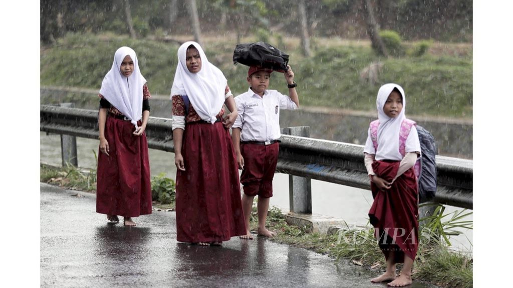 Para siswa sekolah dasar pulang sekolah dengan bertelanjang kaki saat hujan mulai mengguyur kawasan Katulampa, Bogor, Jawa Barat, Kamis (22/8/2019).