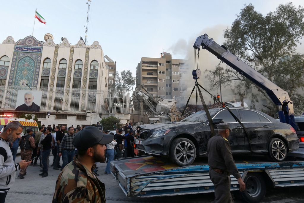 Petugas keamanan memindahkan mobil-mobil yang rusak dari puing-puing gedung di lokasi serangan yang menghantam gedung kedutaan besar Iran di ibu kota Suriah, Damaskus, Senin (1/4/2024). 